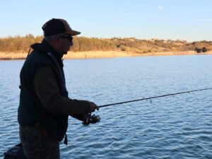 Un pêcheur sur un bateau au lac de la Ganguise en fin de journée avec les lumières du soir sur la berge en arrière plan.