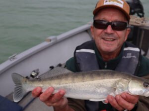 Un pêcheur sur un bateau au lac de la Ganguise qui montre fièrement un sandre qu'il vient d'attraper.
