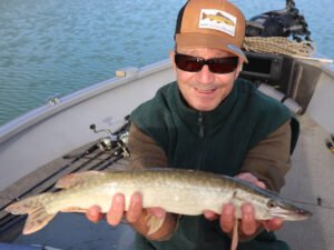 Un pêcheur sur un bateau au lac de la Ganguise qui montre un petit brochet qu'il vient d'attraper.