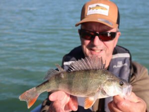Un pêcheur sur un bateau au lac de la Ganguise qui montre une perche qu'il vient d'attraper.