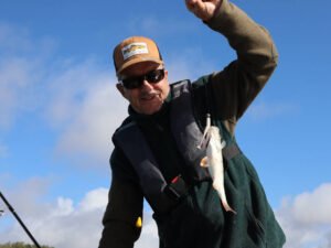 Un pêcheur sur un bateau au lac de la Ganguise qui montre une perche encore accrochée à son leurre.
