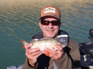 Un pêcheur sur un bateau au lac de la Ganguise qui montre une perche.