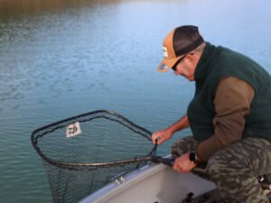 Un pêcheur sur un bateau au lac de la Ganguise qui s'apprête à prendre un poisson dans une épuisete.